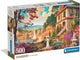 Caja del Puzzle Paseo Victoriano 500 piezas Clementoni. Una mujer con vestido blanco y sombrilla pasea por un jardín florido junto a una casa de piedra y un lago con un velero al atardecer.