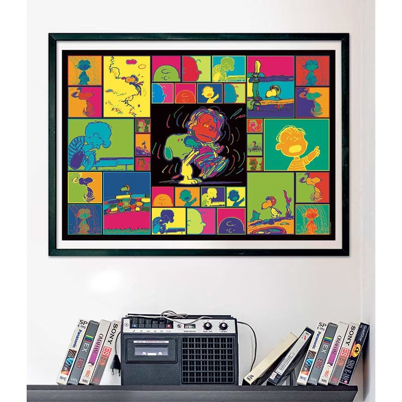 Puzzle Snoopy Peanuts 1000 piezas Clementoni montado y enmarcado en negro sobre una pared, con el collage pop art de los personajes de Peanuts; debajo, un radiocasete y cintas VHS en una estantería.