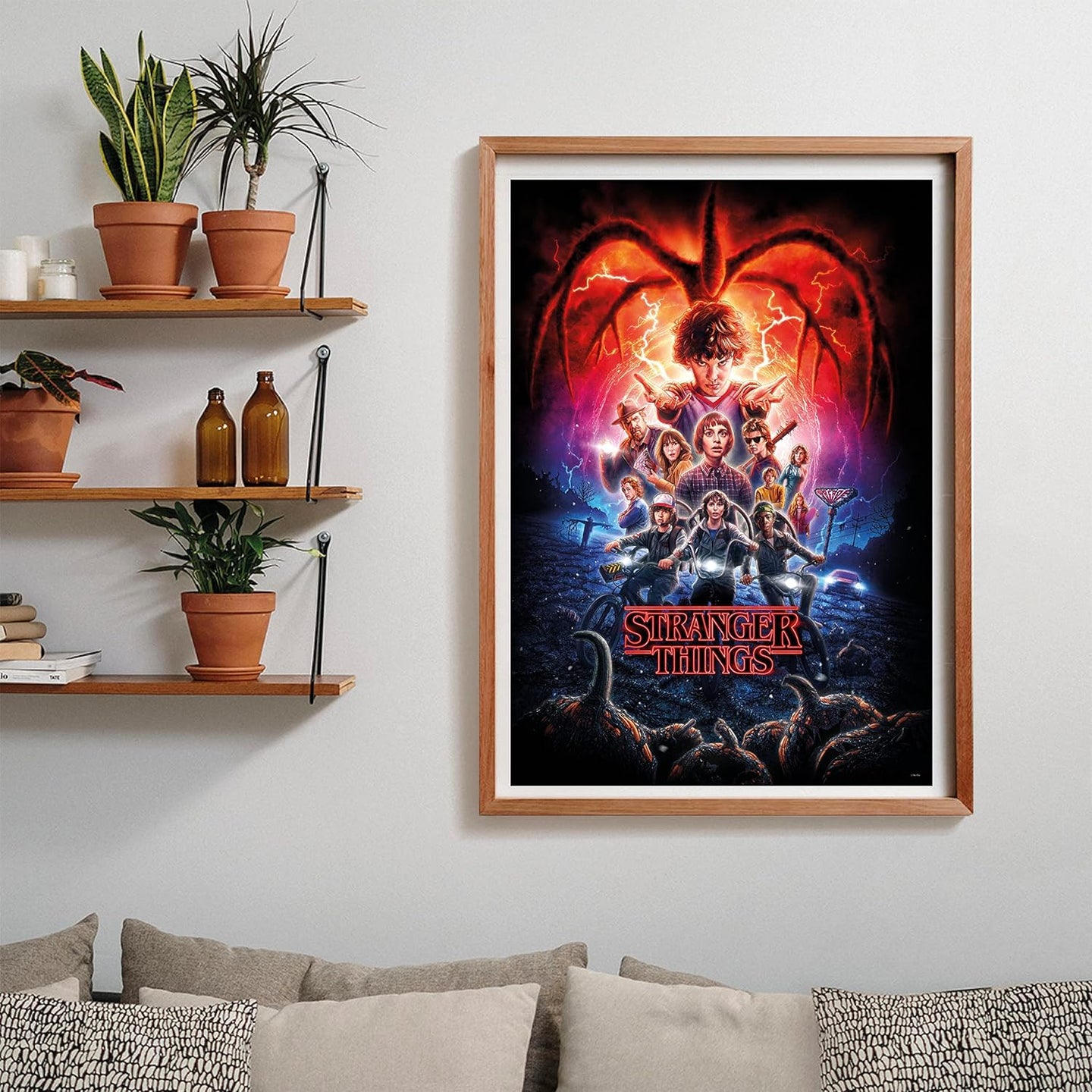 Puzzle Stranger Things Temporada 2 1000 piezas Clementoni montado y enmarcado en madera sobre una pared, con el póster de la serie; al lado, estantes con plantas y libros, y debajo un sofá con cojines.