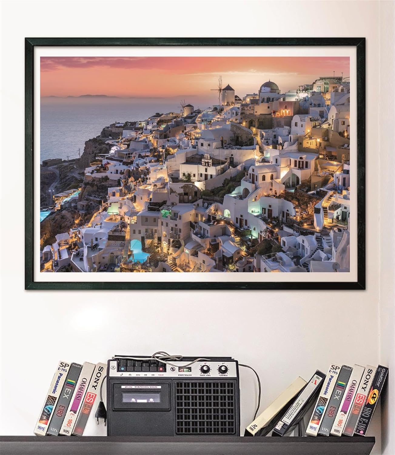 Puzzle Santorini 1000 piezas Clementoni montado y enmarcado en negro sobre pared, sobre un estante con cintas VHS y radio-casete vintage