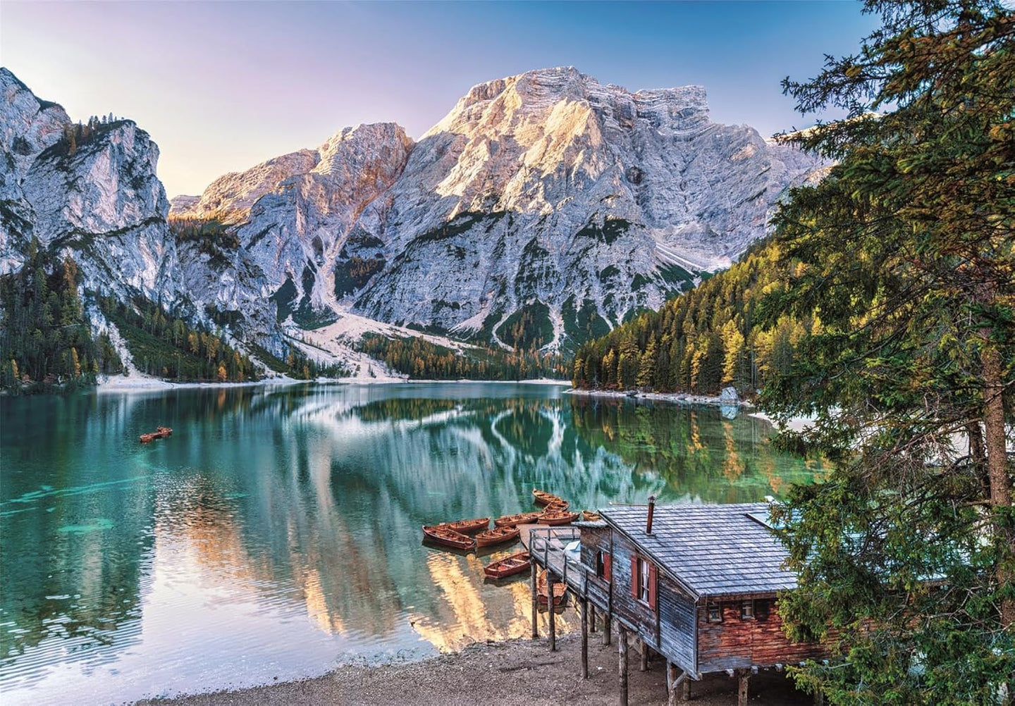 Ilustración del puzzle Lago Esmeralda 1000 piezas Clementoni con un lago de aguas turquesa entre montañas alpinas, una cabaña de madera y barcas amarradas