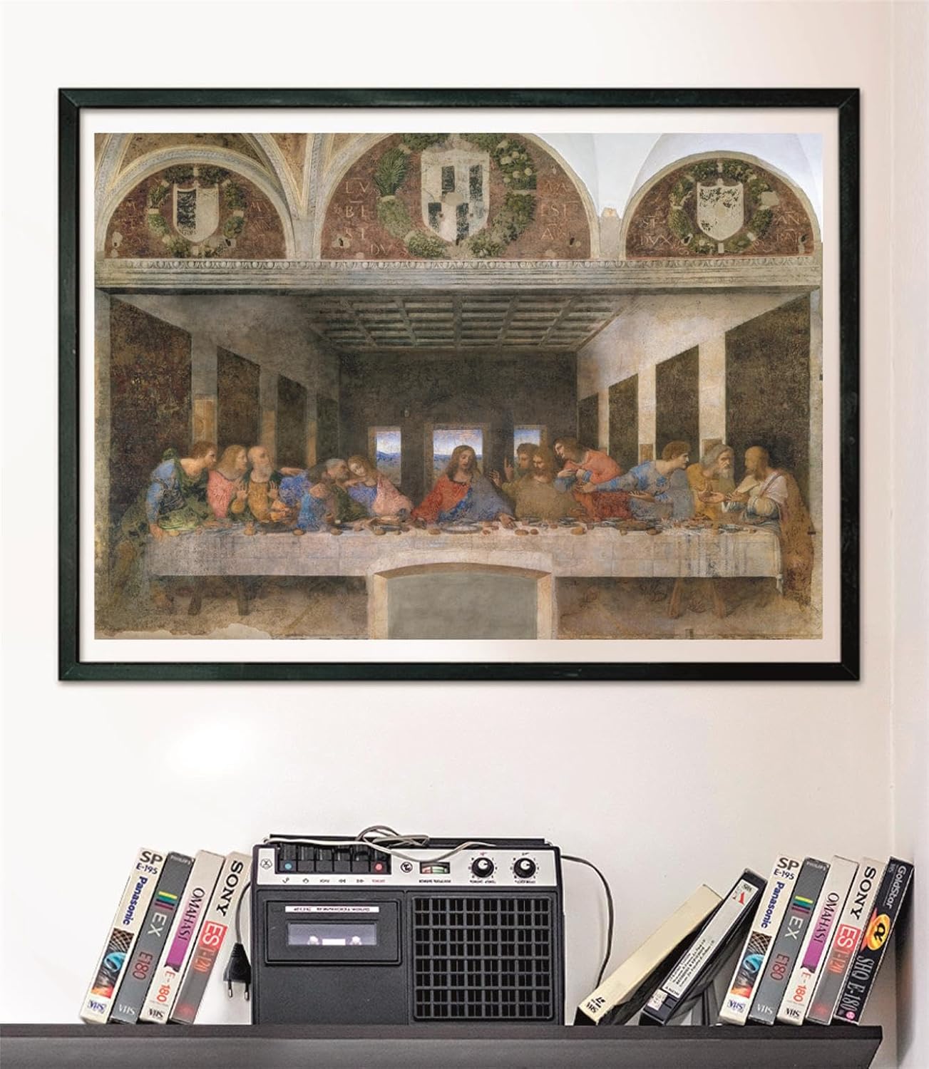 Puzzle La Última Cena de Leonardo 1000 piezas Clementoni Museum Collection montado y enmarcado en negro sobre pared, sobre un estante con cintas VHS y radio-casete vintage