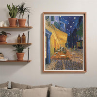 Puzzle Terraza de Café por la Noche Van Gogh 1000 piezas Clementoni montado y enmarcado en madera clara sobre pared, junto a estanterías con plantas y sofá con cojines