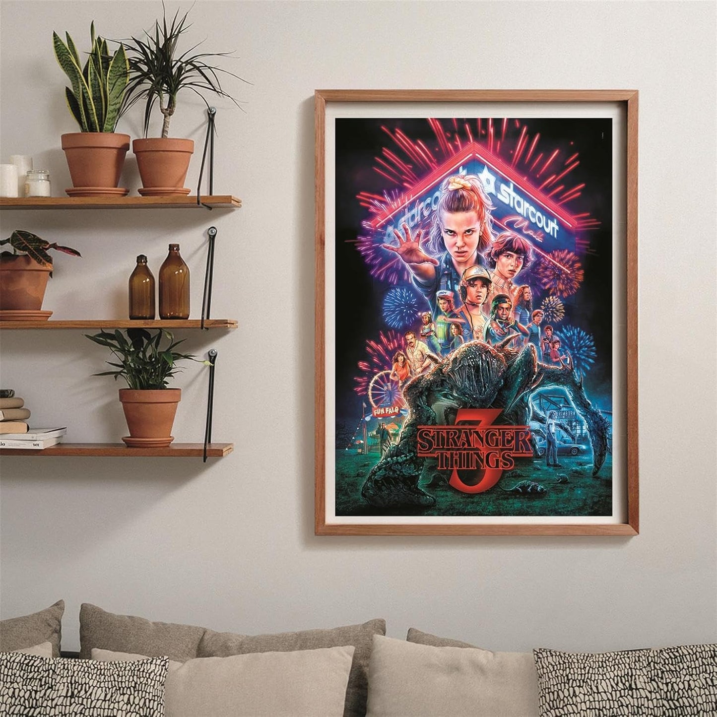 Puzzle Stranger Things Temporada 3 1000 piezas Clementoni montado y enmarcado en madera sobre una pared, con el póster de la serie; al lado, estantes con plantas y libros, y debajo un sofá con cojines.
