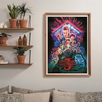 Puzzle Stranger Things Temporada 3 1000 piezas Clementoni montado y enmarcado en madera sobre una pared, con el póster de la serie; al lado, estantes con plantas y libros, y debajo un sofá con cojines.