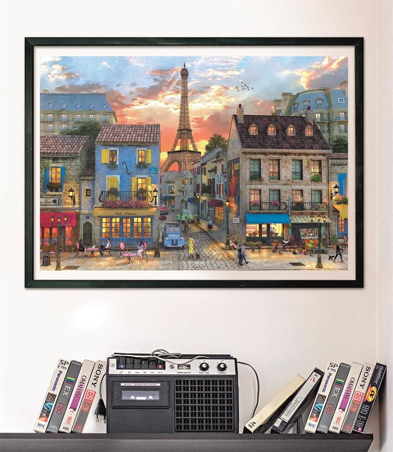 Puzzle Calle de París 1000 piezas Clementoni montado y enmarcado en negro sobre pared, sobre un estante con cintas VHS y radio-casete vintage