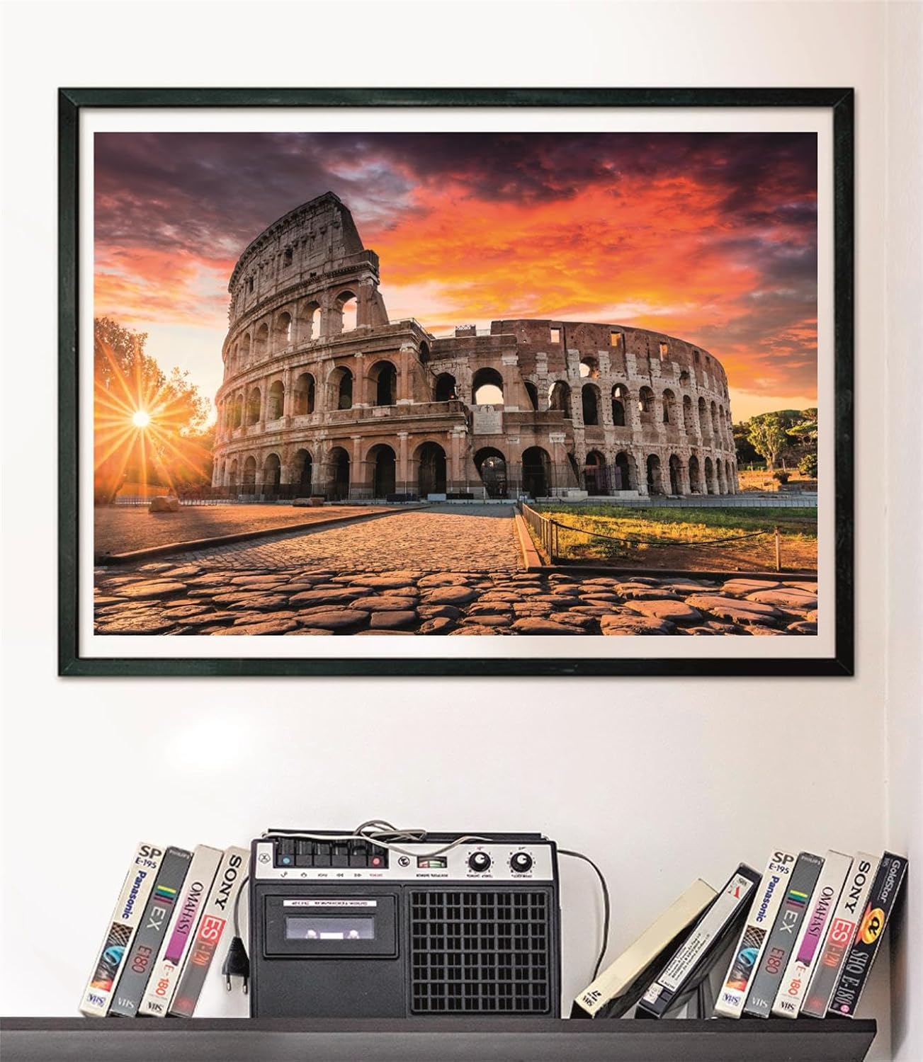 Puzzle Atardecer en el Coliseo de Roma 1000 piezas Clementoni montado y enmarcado en negro sobre pared, sobre un estante con cintas VHS y radio-casete vintage